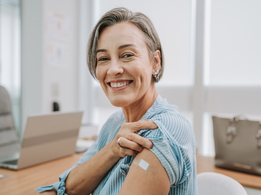 Frau zeigt Impfpflaster auf ihrem Oberarm